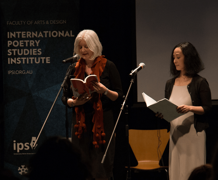 Melinda Smith (right) and Harumi Kawaguchi (left) reading in front of microphones.